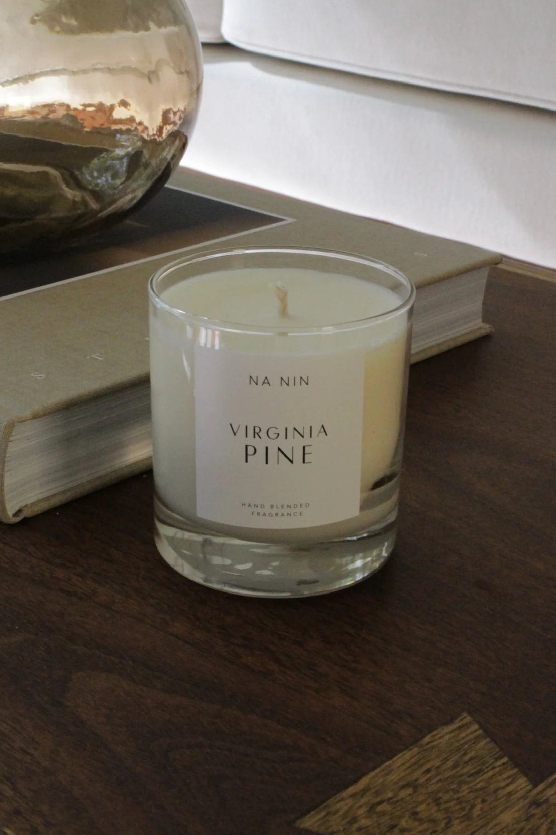 Candle labeled 'Virginia Pine' on a wooden surface with a gold decorative object and books in the background.